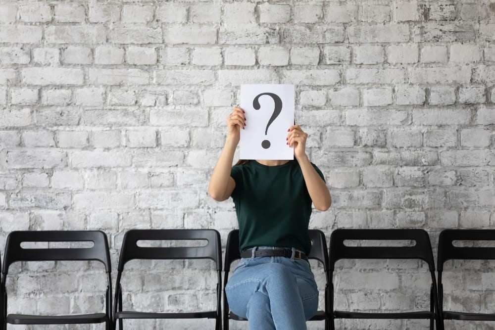 Young woman candidate hiding face behind sheet with question mark